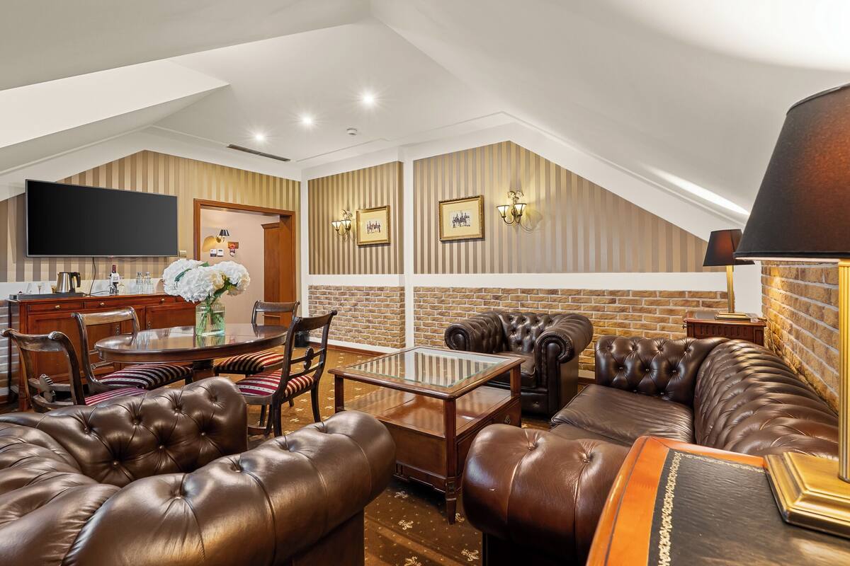 A spacious living area with a high ceiling, leather sofas, a glass-top coffee table, and a flat-screen TV mounted on the wall.