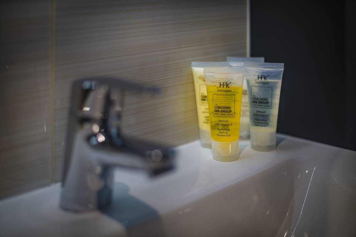 A bathroom sink with toiletries including a Harrogate shampoo and a H2K conditioner.