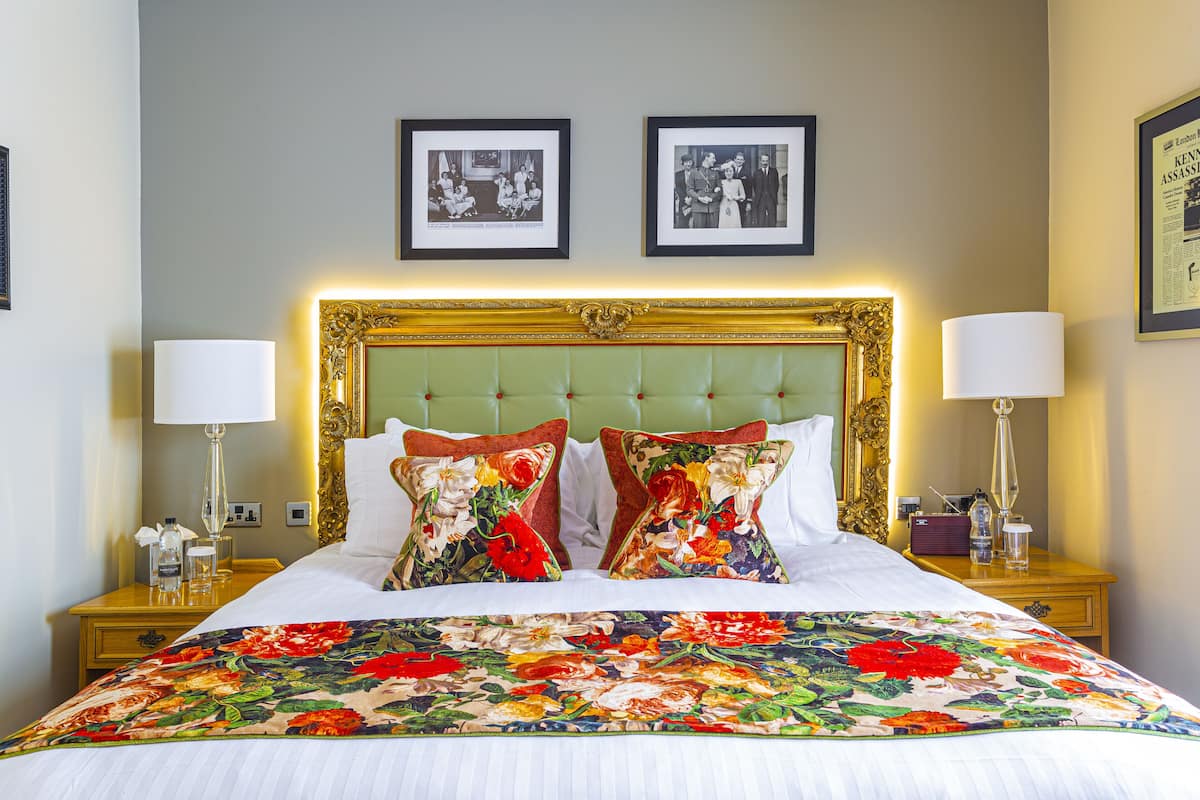 A neatly made bed with a floral bedspread, a green upholstered headboard, and two framed photographs on the wall above.