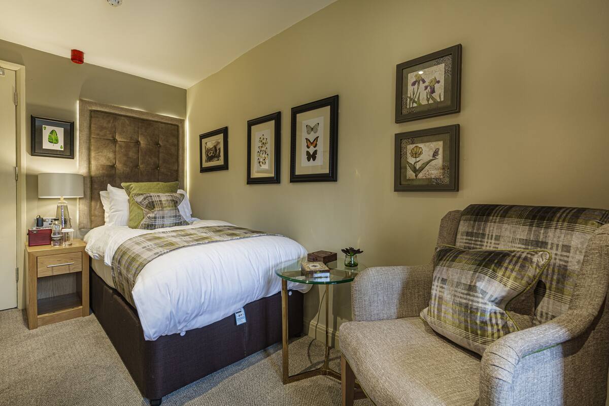 A hotel room with a bed, a chair, a small table, and framed pictures on the wall.