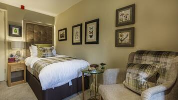 A hotel room with a bed, a chair, a small table, and framed pictures on the wall.