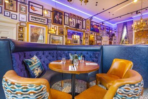 A restaurant with a blue upholstered booth, a round wooden table, and orange chairs.