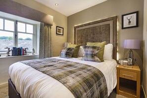 A neatly made bed with a plaid bedspread, a bedside lamp, and a nightstand with a lamp and a glass.