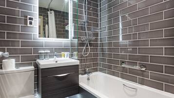 Un baño moderno con lavamanos blanco, tocador de madera oscura y bañera blanca.