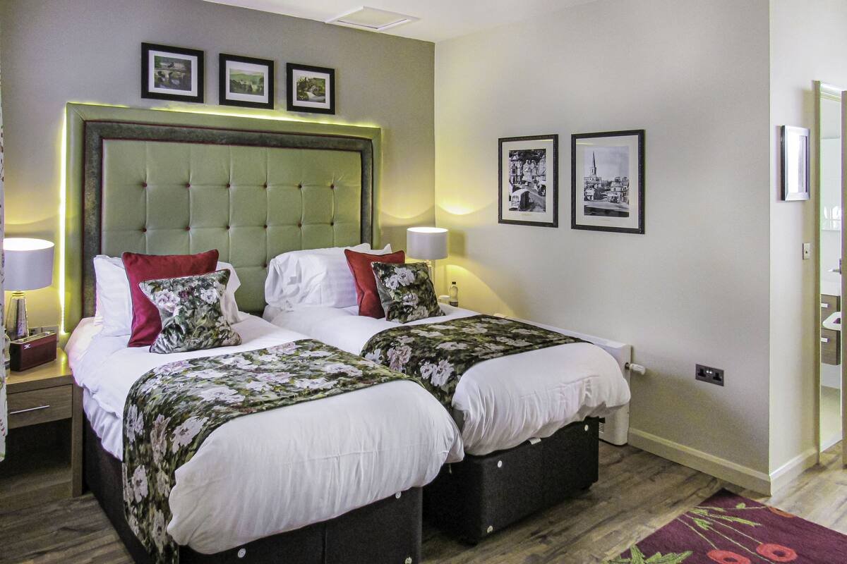 A hotel room with two beds, a large headboard, and framed pictures on the wall.