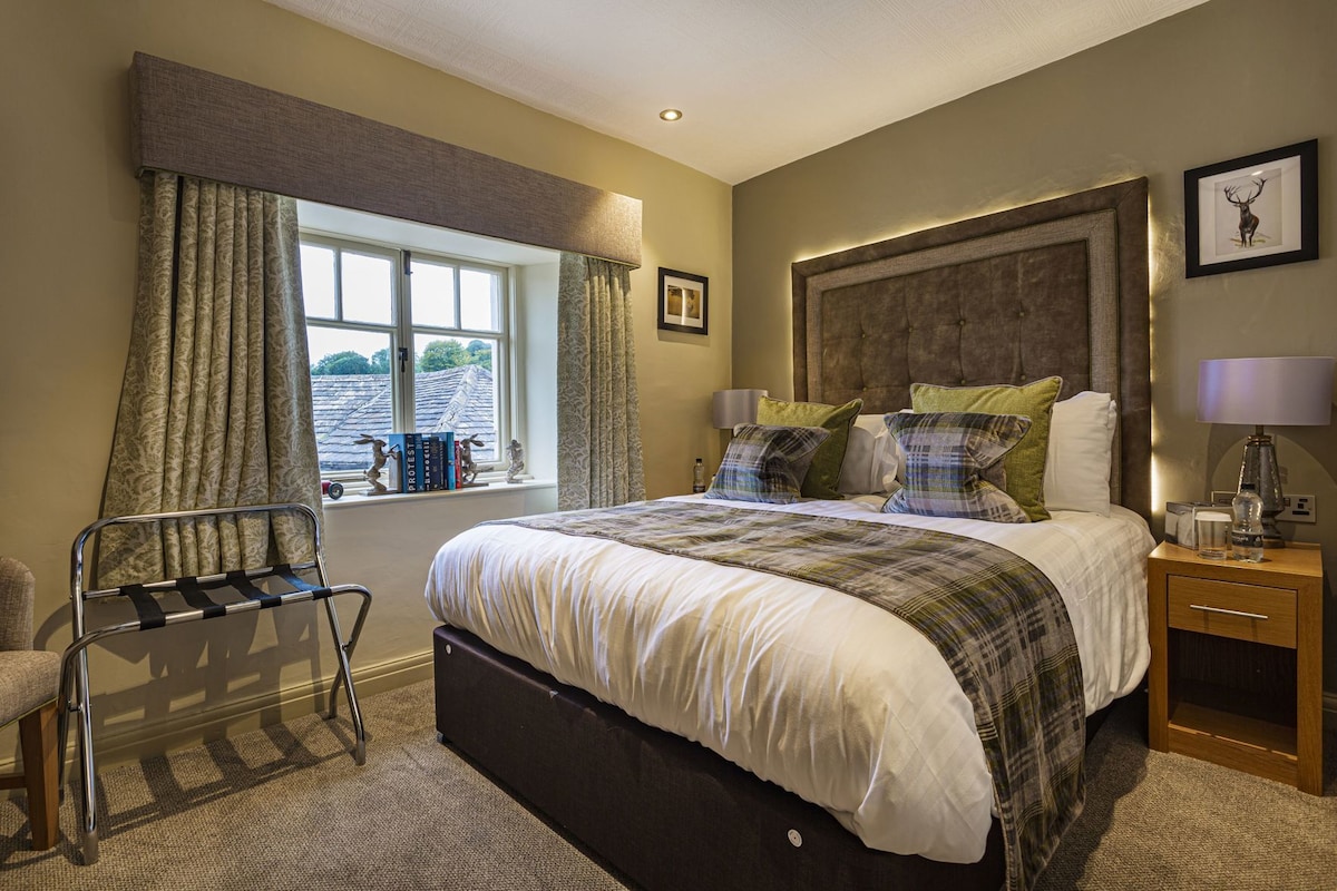 A bedroom with a large bed, a bedside table with a lamp, a window with curtains, and a chair.