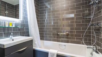 Un baño moderno con pared de azulejos oscuros, una bañera blanca y un tocador con espejo.