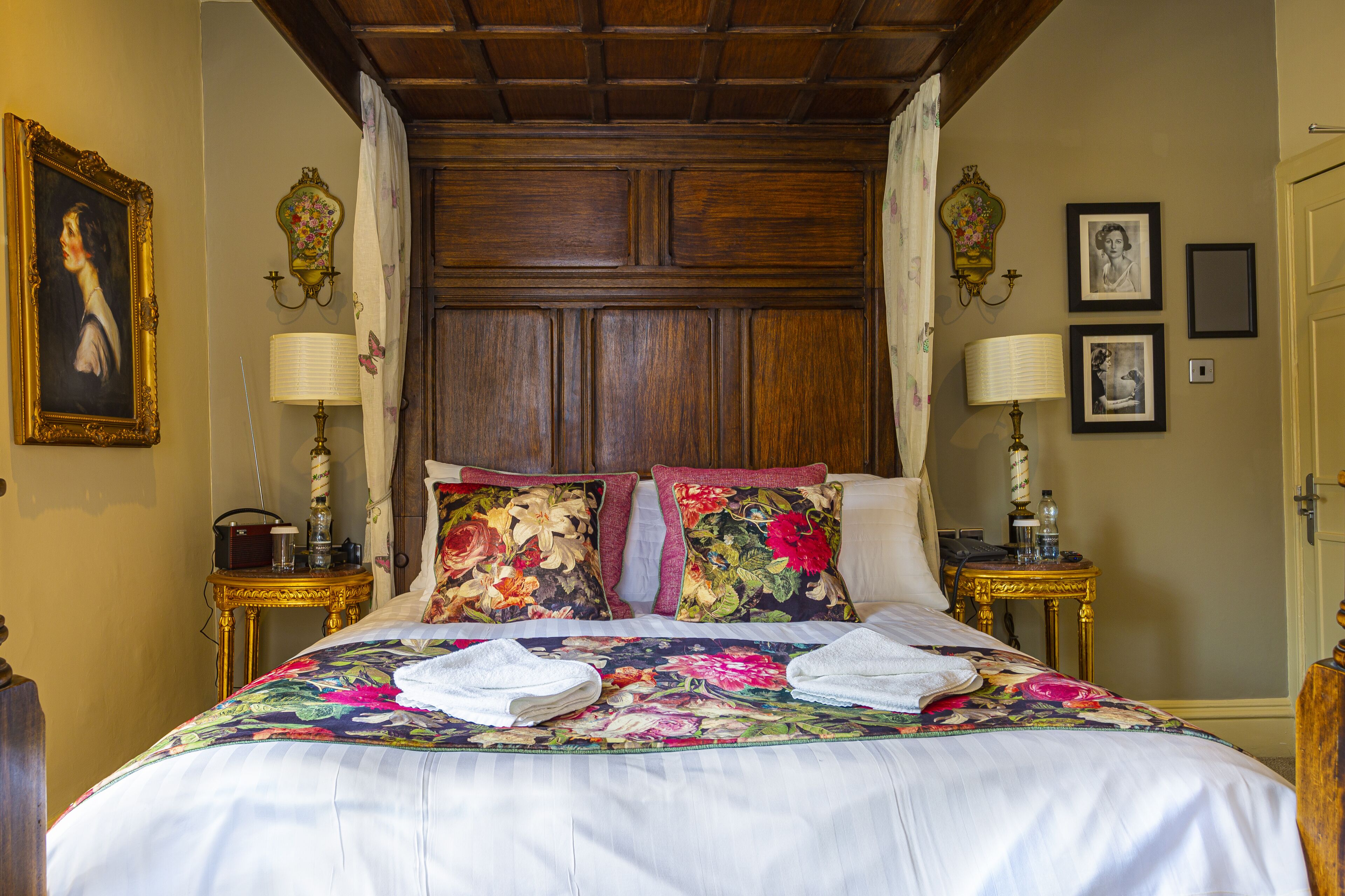 A neatly made bed with floral bedding, two lamps on nightstands, and framed pictures on the wall.