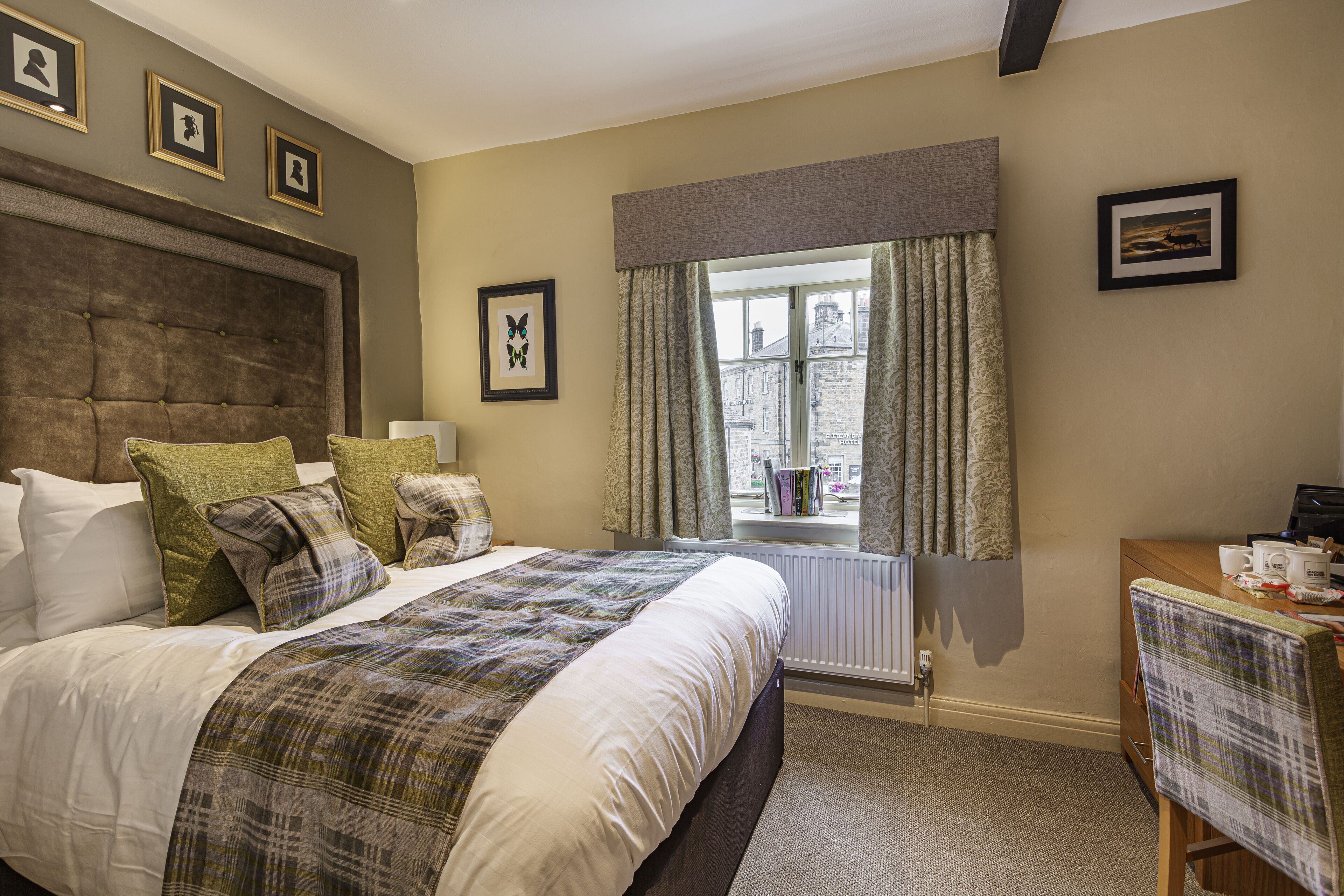A neatly arranged bedroom with a large bed, a window with curtains, a desk, and framed pictures on the walls.