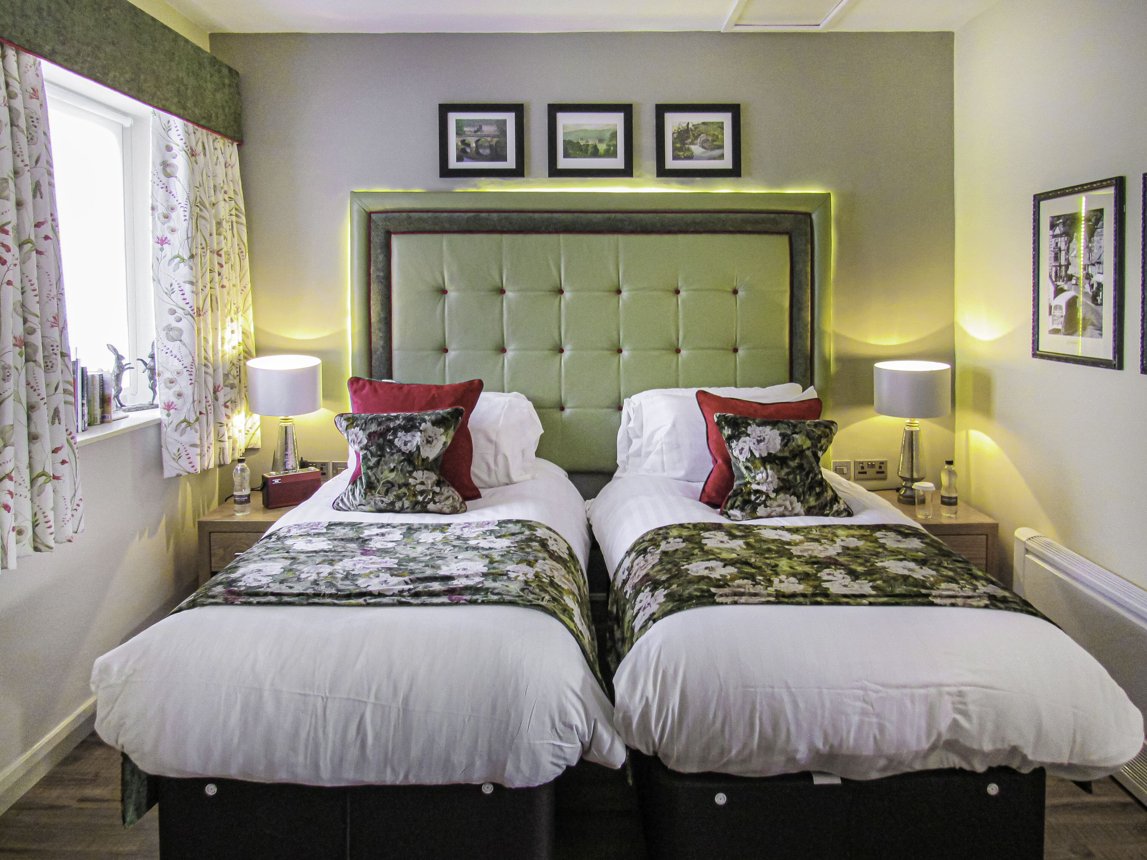 A hotel room with two beds, a large green headboard, and three framed pictures on the wall.