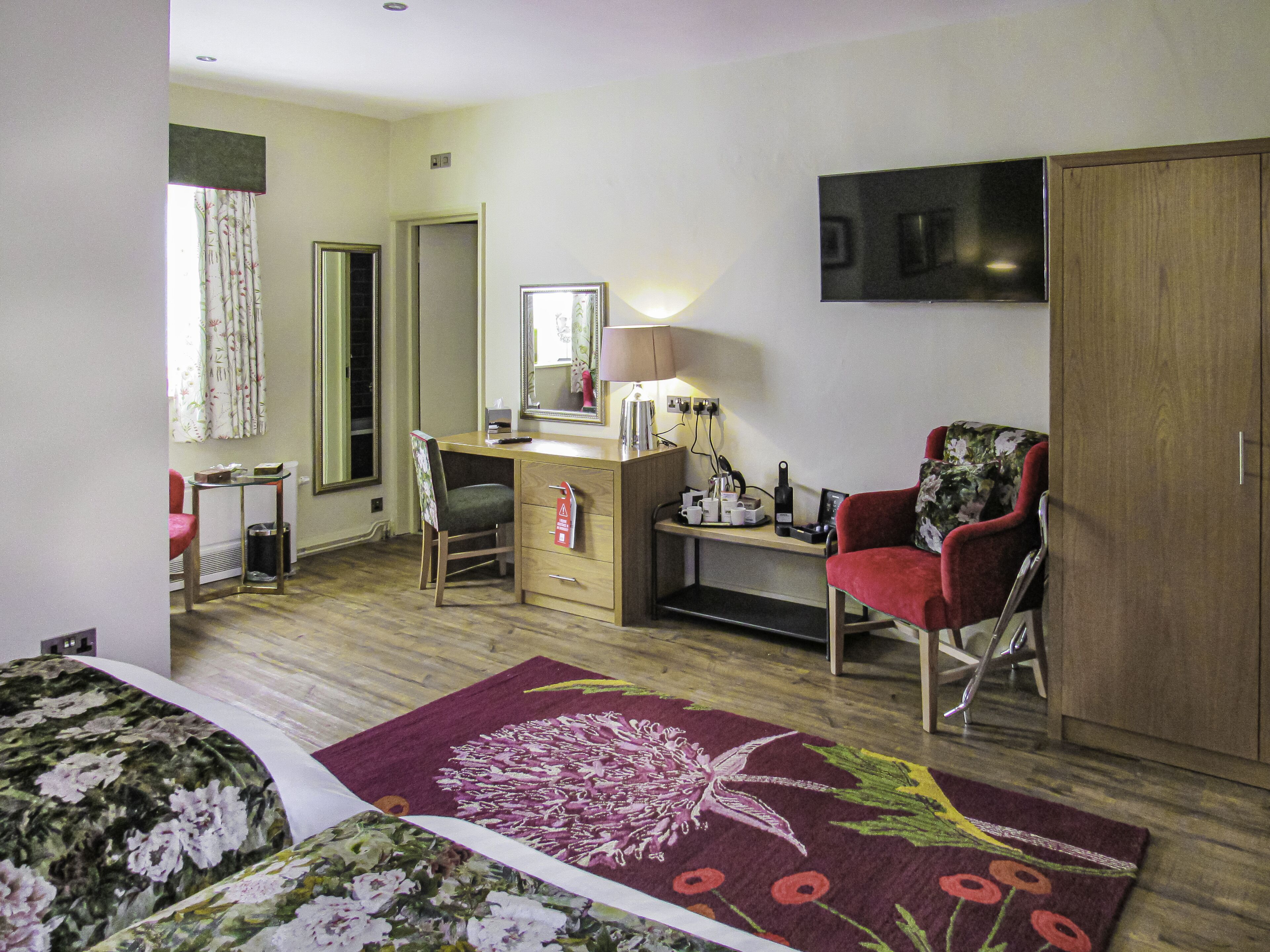 A hotel room with a bed, a desk, a chair, a wardrobe, and a large mirror.