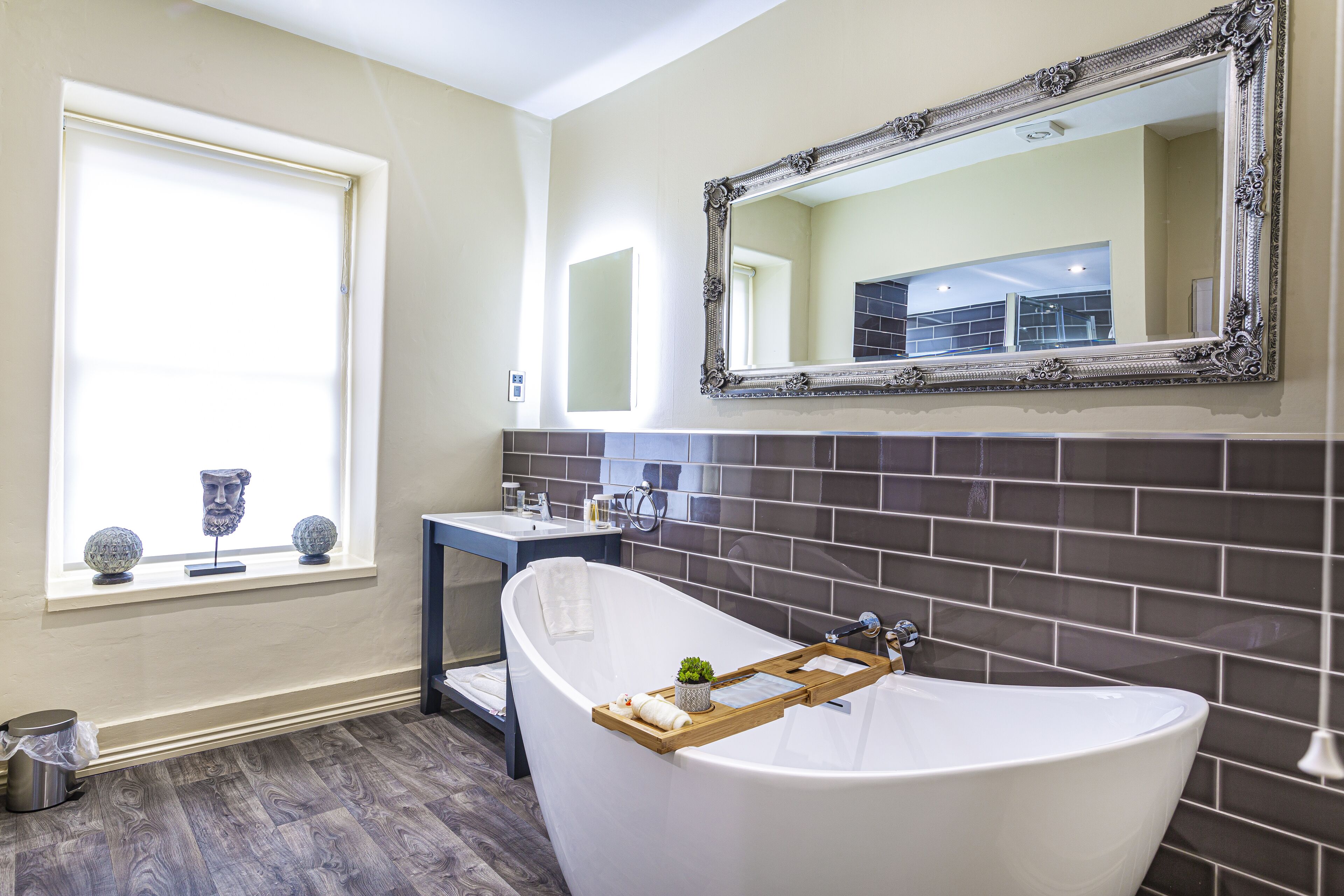 A bathroom with a freestanding bathtub, a vanity with a mirror, and a window with decorative items.
