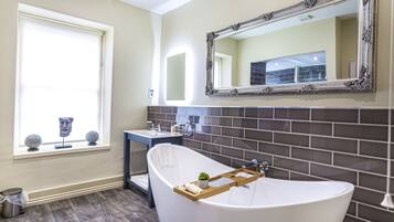 A bathroom with a freestanding bathtub, a vanity with a mirror, and a window with decorative items.