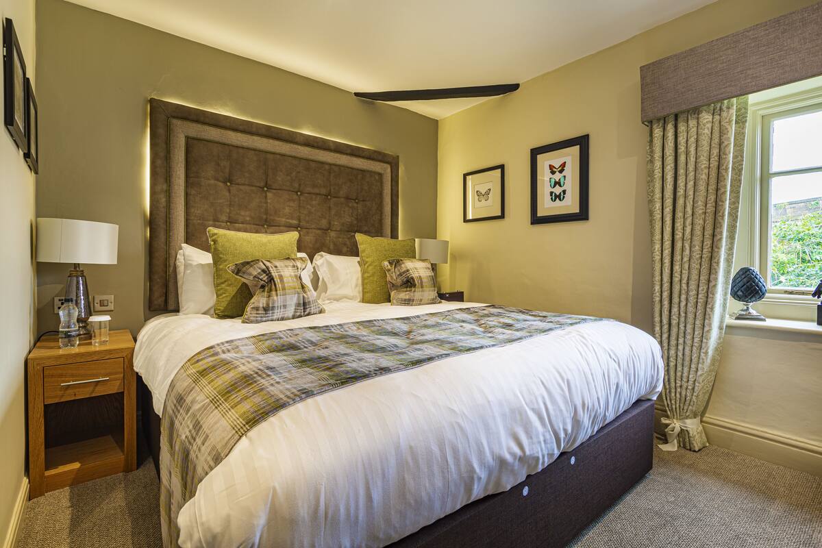 A neatly made bed with a plaid bedspread, a wooden nightstand with a lamp, and two framed butterfly pictures on the wall.