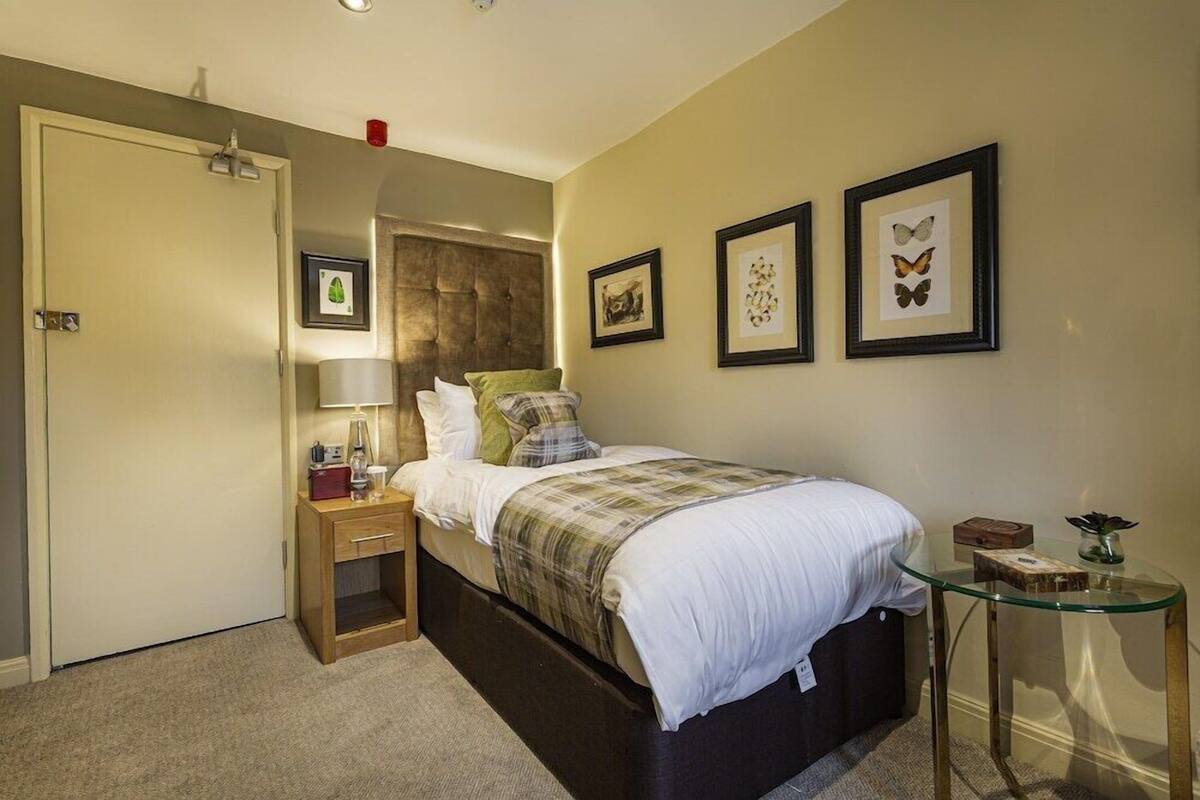 A bedroom with a bed, bedside table, lamp, and wall art.