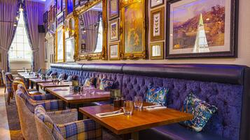 A restaurant with a long counter, plush seating, and framed artwork on the walls.