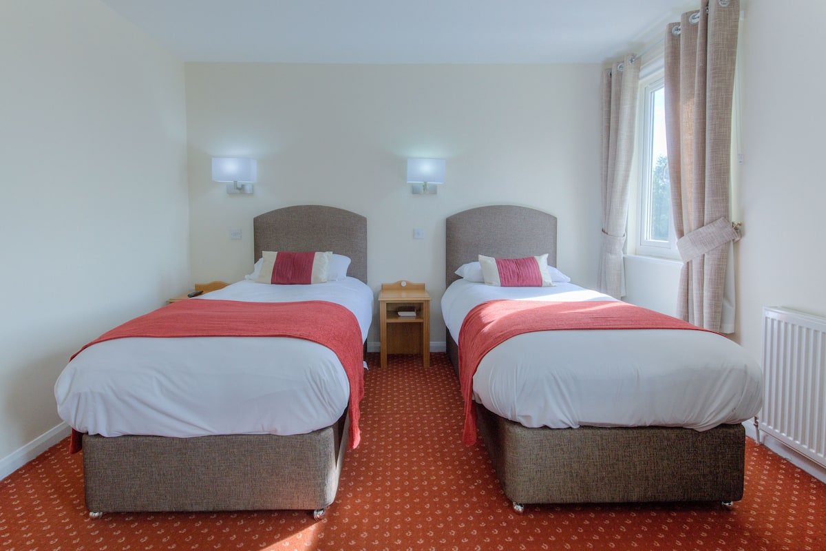 A hotel room with two beds, each with a headboard, a nightstand, and a lamp.