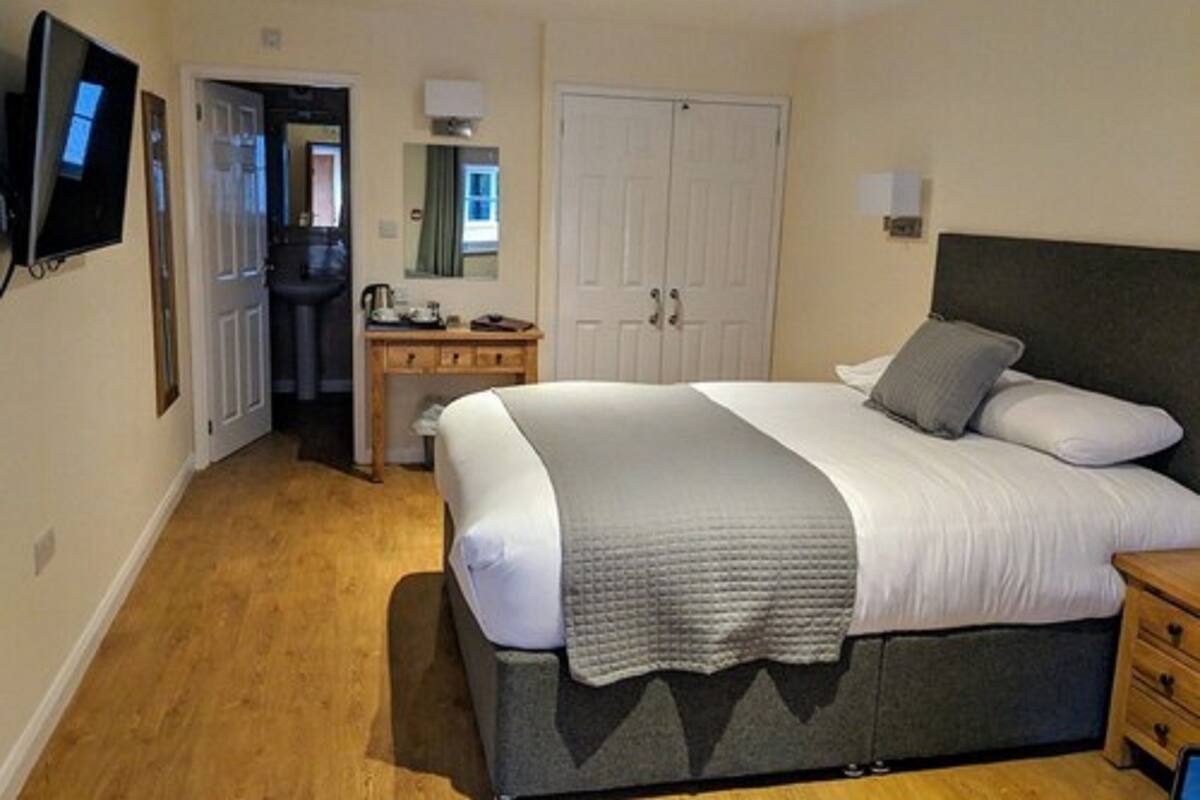 A bedroom with a bed, bedside table, dresser, and a television mounted on the wall.