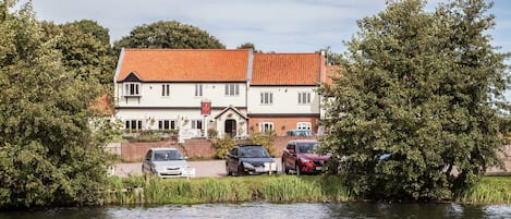 A two-story building with a red-tiled roof, parked cars in front, and a body of water in the foreground.