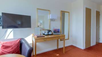 A hotel room with a desk, a flat-screen TV, a large mirror, and a red carpeted floor.
