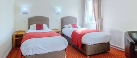 Una habitación de hotel con dos camas, una mesita de noche, una silla y una ventana con cortinas.