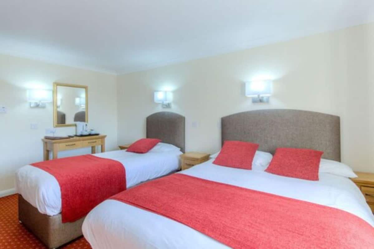 A hotel room with two beds, each with a red blanket, a bedside table with a lamp, and a mirror on the wall.