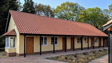 Situated on a paved area, this charming building features a red-tiled roof and a yellow facade with a central door and side windows.