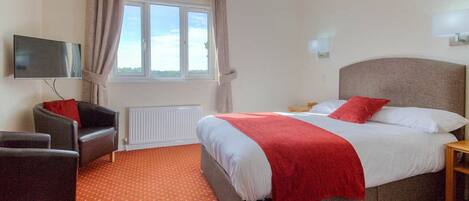 A hotel room with a bed, a TV, a chair, and a window.