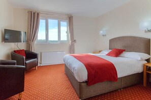 A hotel room with a bed, a TV, a chair, and a window.