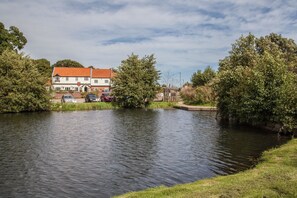 A riverside building with a red roof, surrounded by trees and parked cars.