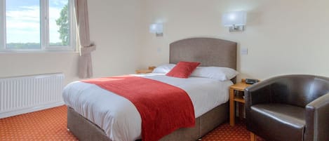 A hotel room with a bed, a chair, a nightstand, and a window with curtains.