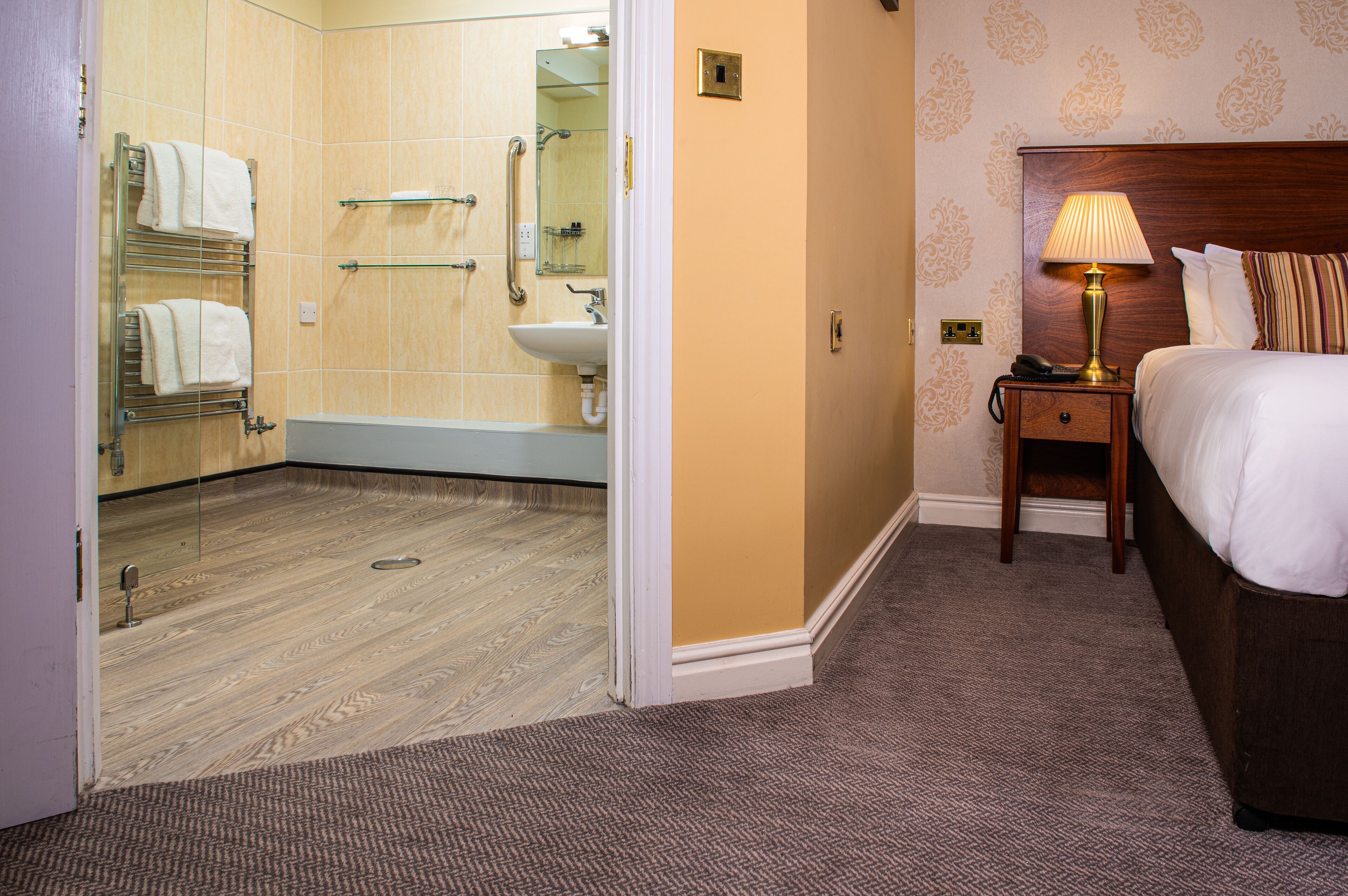 A hotel room with a bathroom, a bed, a nightstand, and a lamp.
