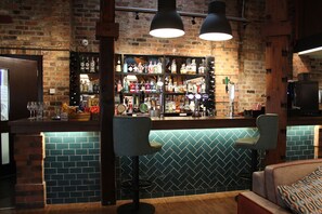 A bar area with a brick wall, shelves of liquor bottles, two bar stools, and a counter. - Middletons Hotel (York)