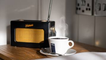 Une tasse de café posée sur une soucoupe, avec une cuillère, une radio ancienne et une prise électrique en arrière-plan.