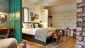 A cozy bedroom with a bed, a wooden desk, a chair, and a small table with a plant.