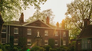 A brick building with a central entrance, surrounded by greenery and trees.