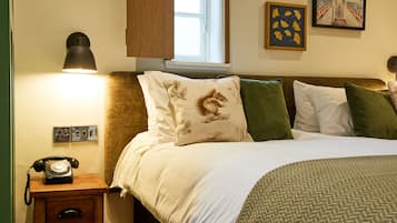 Een opgemaakt bed met gestreepte kussens, een bedlamp en een klassieke telefoon op een houten nachtkastje.