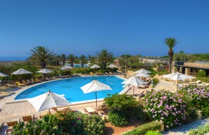 A swimming pool with sun loungers and umbrellas, surrounded by greenery and a clear view of the sea. - Hotel Ta' Cenc & Spa (Sannat)