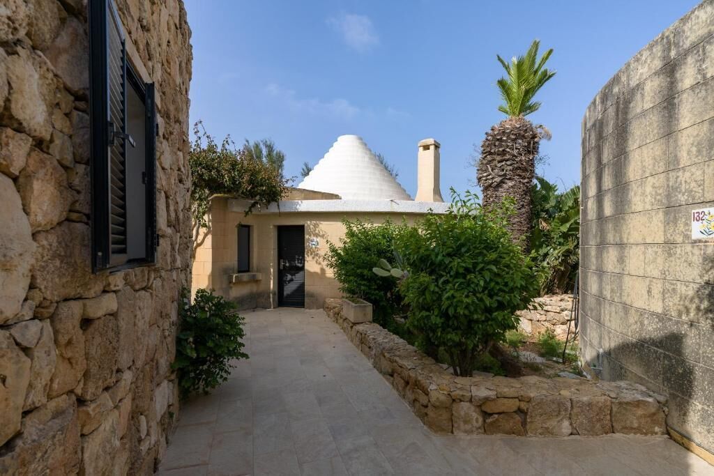 A narrow stone pathway leading to a building with a conical roof and a chimney.