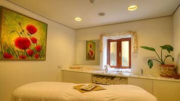 A hotel bathroom with a bed, a large mirror, a window with curtains, a sink, and a potted plant.