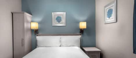 A neatly made bed with white linens, two bedside lamps, and two framed artworks on the wall.