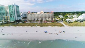 Ein Strandhotel mit mehreren Etagen, ein Sandstrand davor und freie Sicht auf den Ozean.