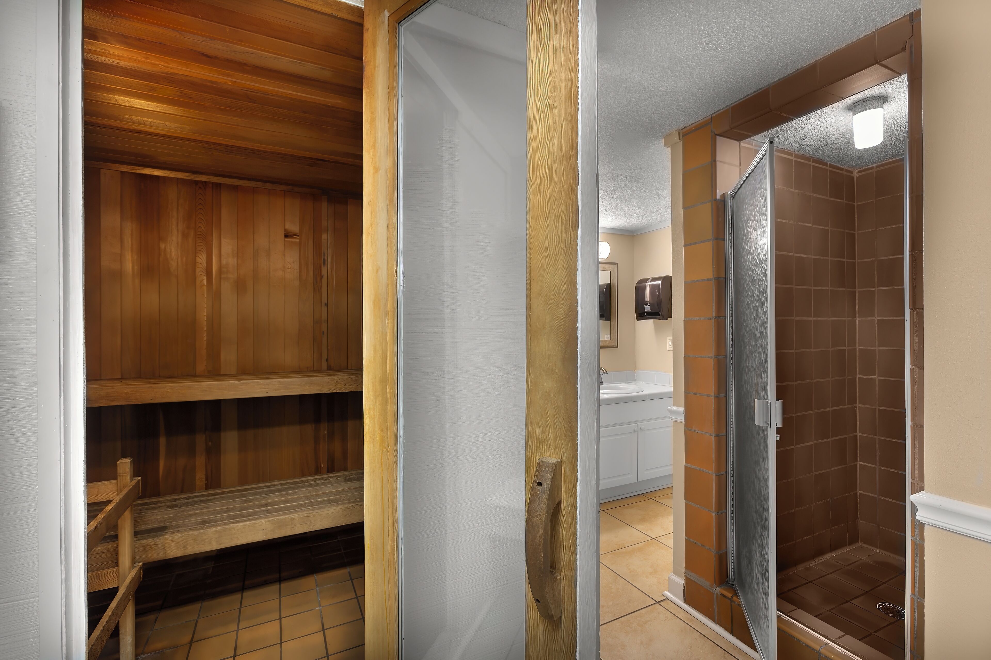 Un sauna en bois avec des bancs, une cabine de douche en verre et un lavabo blanc.