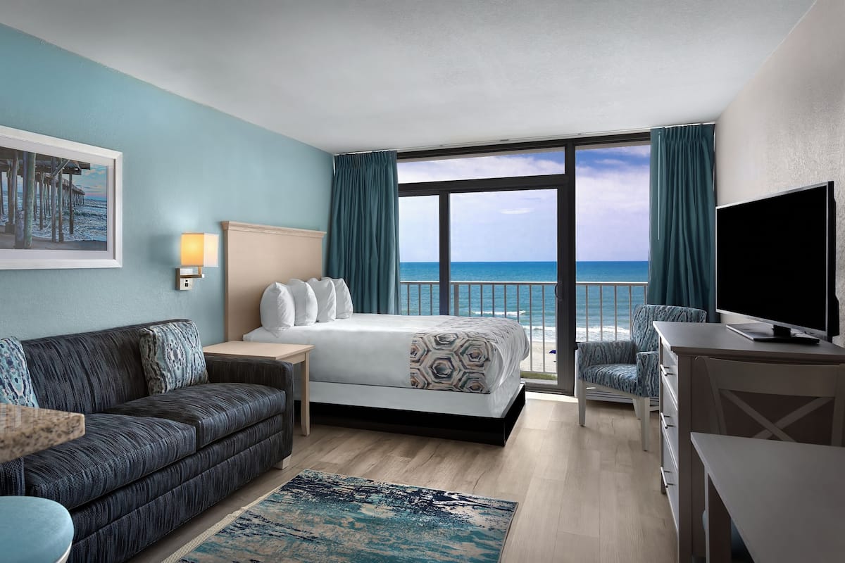 A hotel room with a bed, a sofa, a desk, a TV, and a view of the ocean.