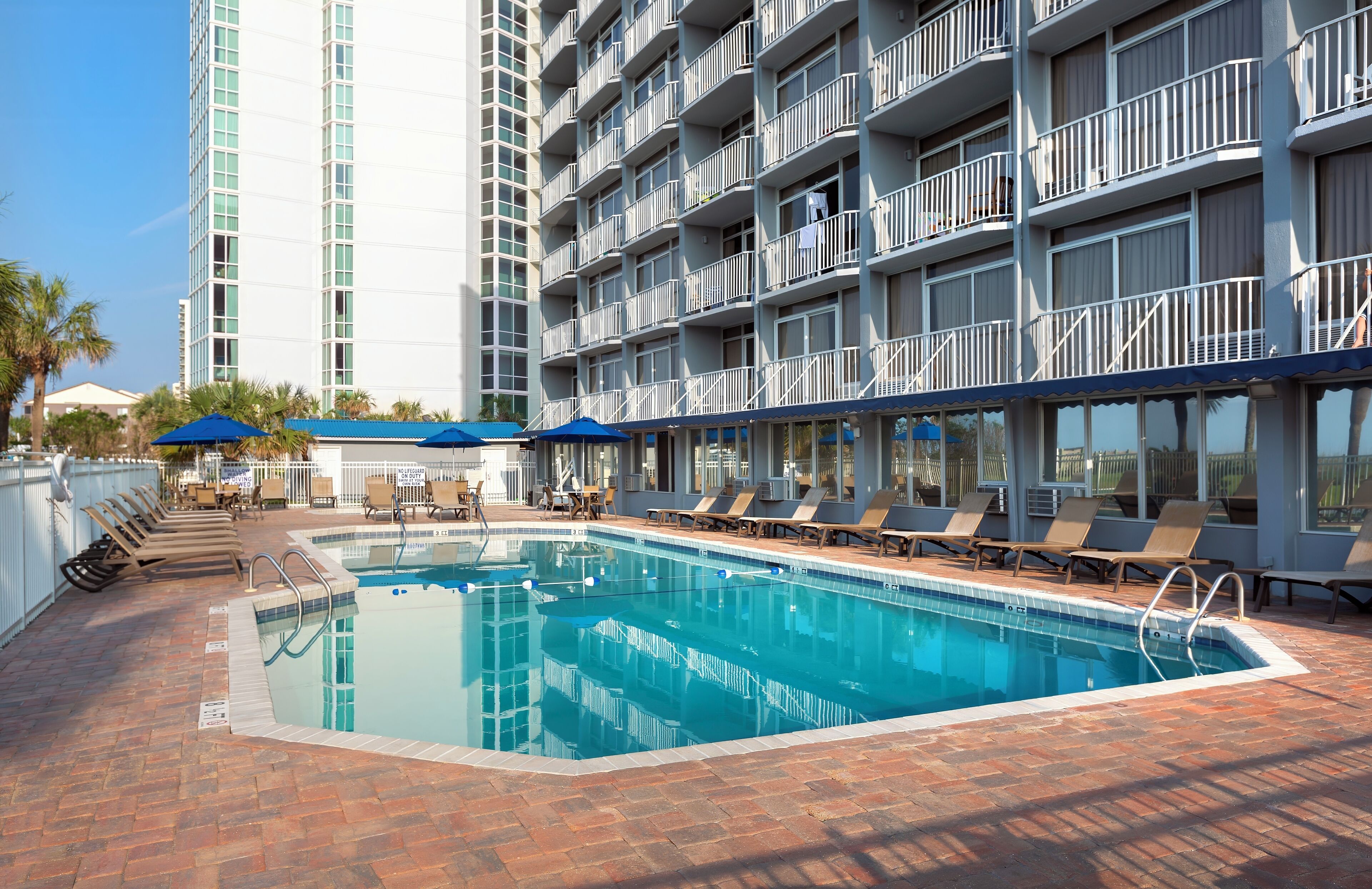 A swimming pool area with lounge chairs and umbrellas, surrounded by a multi-story building with balconies.