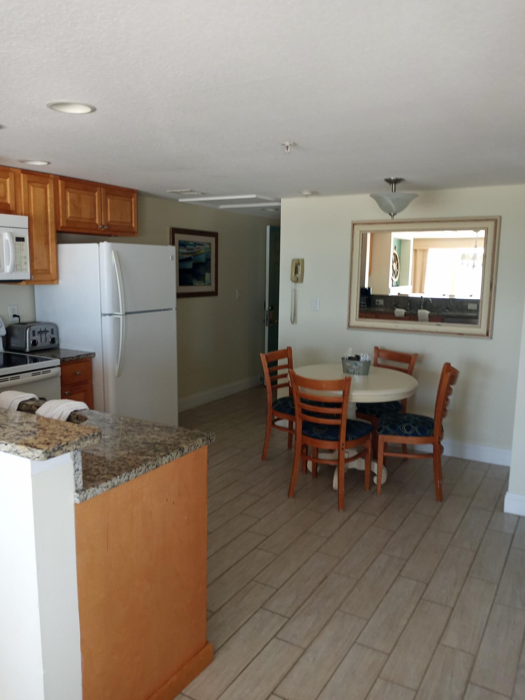 Una cocina con armarios de madera, un refrigerador, un microondas, un tostador y un comedor con mesa y sillas.