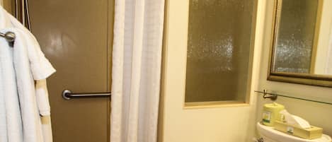 Un baño con ducha, inodoro y un estante de vidrio con artículos de aseo.