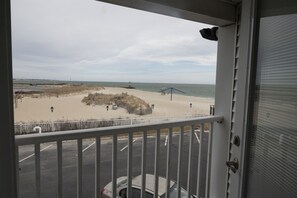 A balcony with a view of a beach, a fence, and a parking area. - Ocean Club on Smuggler's Beach (South Yarmouth)
