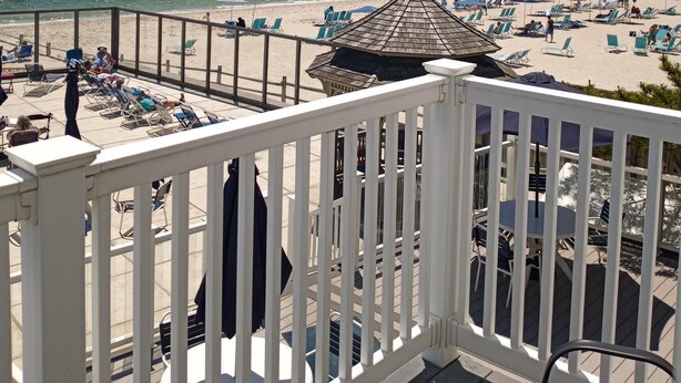 Une vue sur la plage depuis un balcon doté d’une balustrade, avec des chaises de plage, des parasols et un petit kiosque.