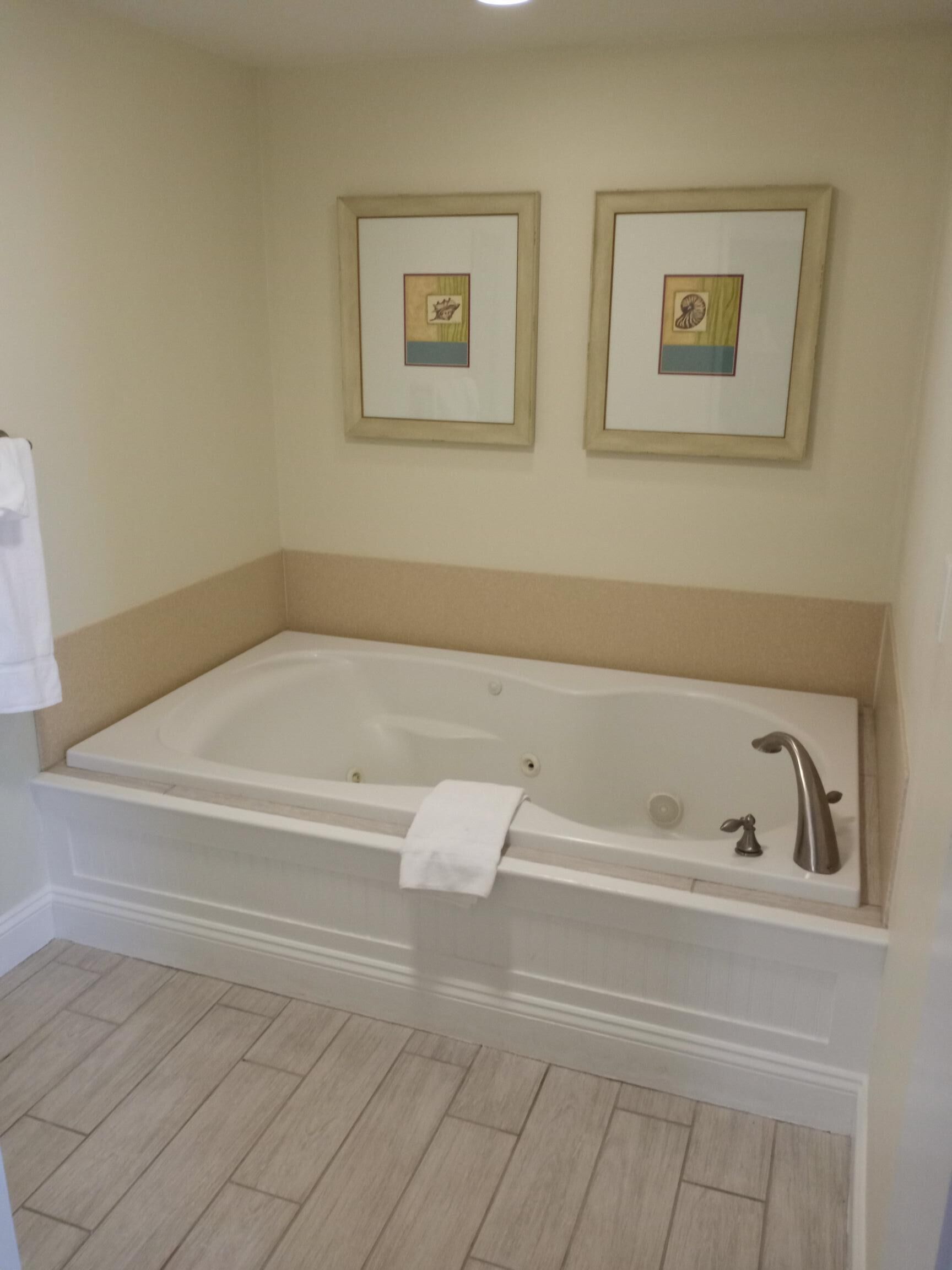 A bathroom with a large bathtub, two framed pictures on the wall, and a white towel hanging on the side.